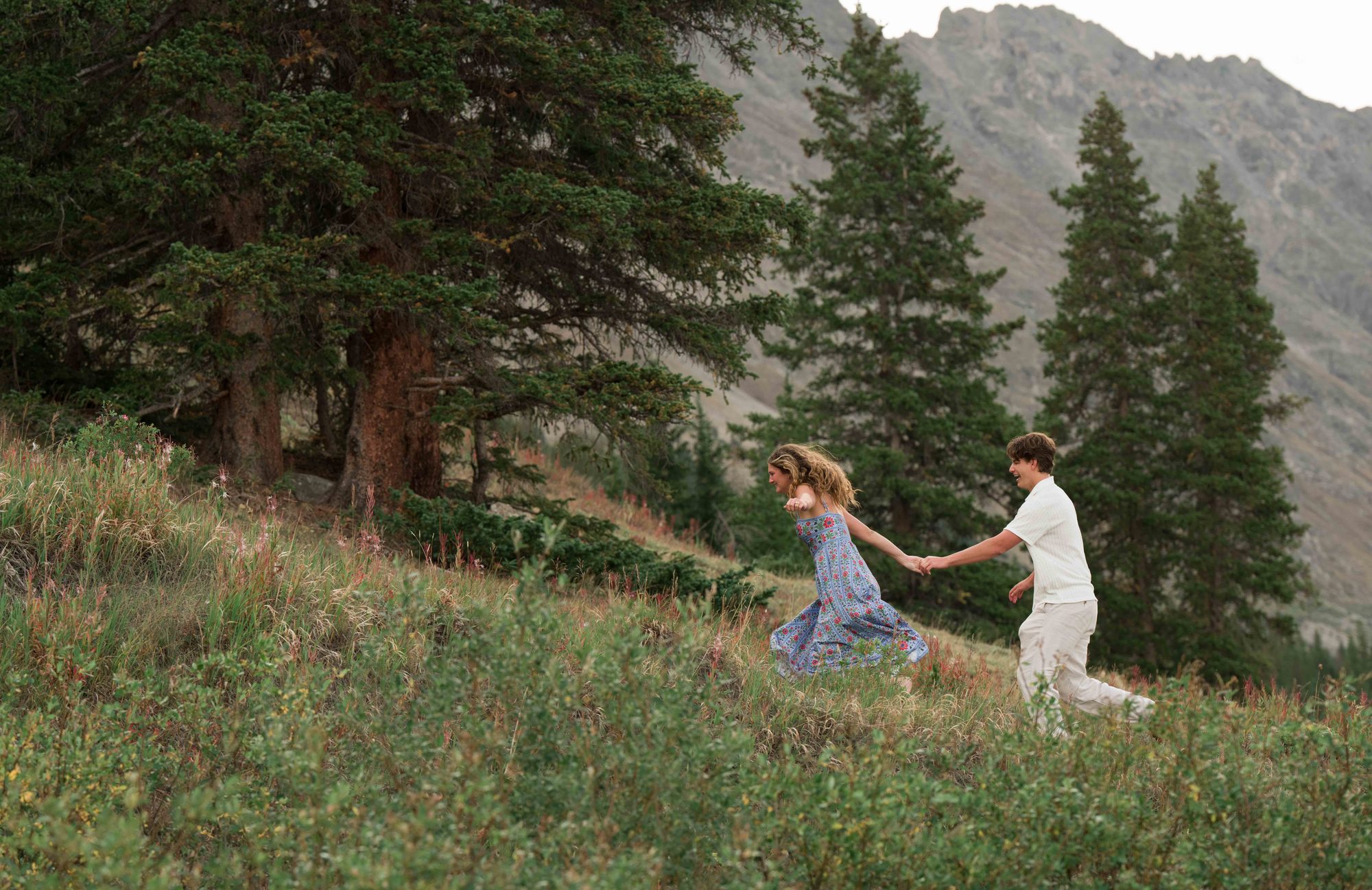 Anna leading Brock by the hand up a mountain meadow